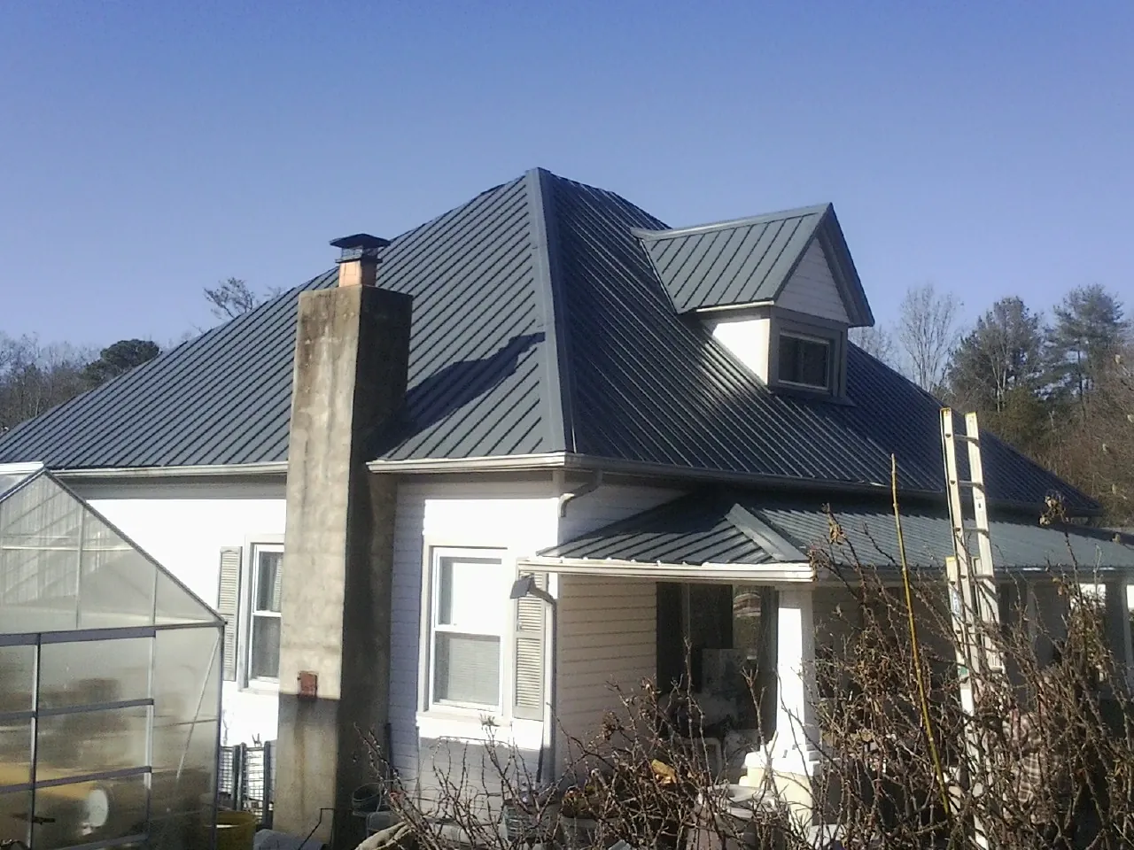 Dark blue standing seam metal roof on a white farmhouse with dormer — Slate & Tile Roof Repair by Roofing Brothers in Hamptonville
