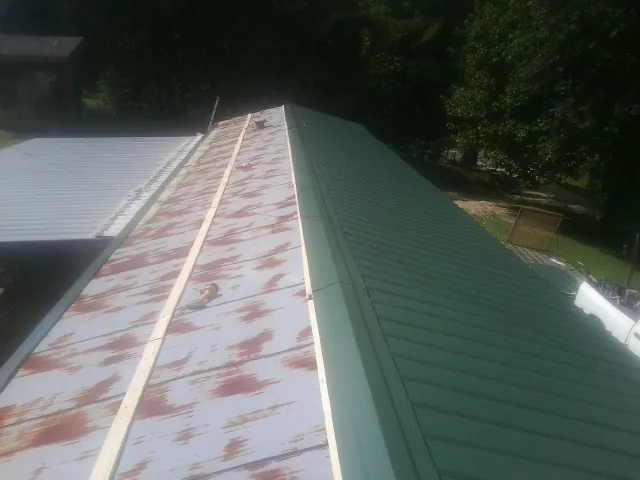 Old rusted panels beside newly installed green metal roofing — Wind Damage Roof Repair by Roofing Brothers in Hamptonville