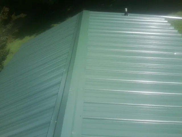 New green metal panels meeting at the ridge of a roof — Flat Roof Repair work by our crew in Hamptonville