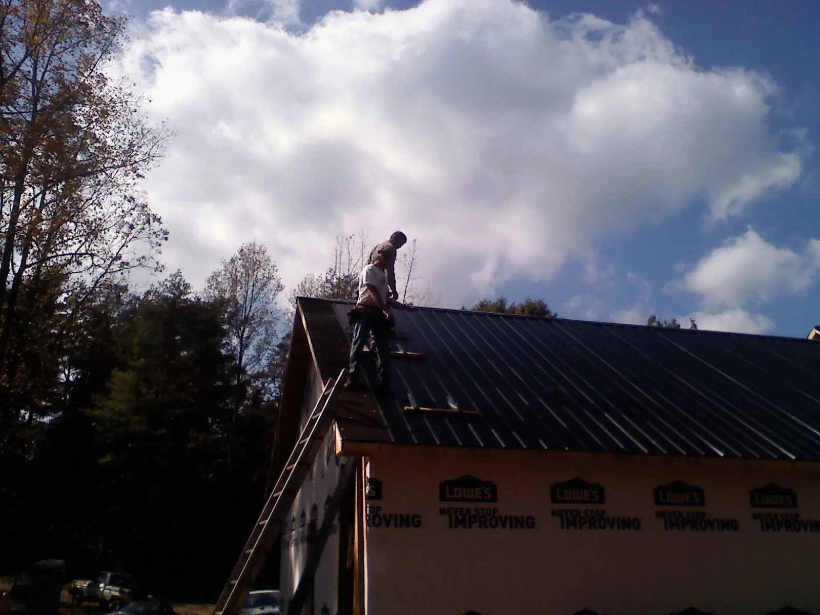 Roofer fastening dark metal panels high against a cloudy sky, from a Roof Inspection job in Hamptonville