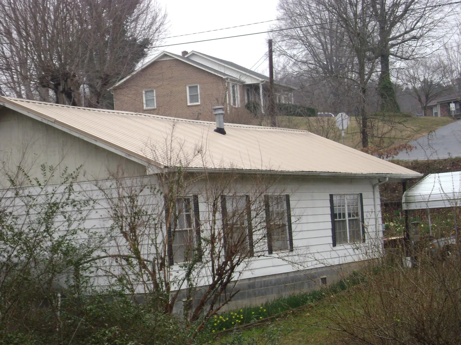 Tan metal roof on a white sided house set into a hillside — Commercial Roofing by Roofing Brothers in Hamptonville