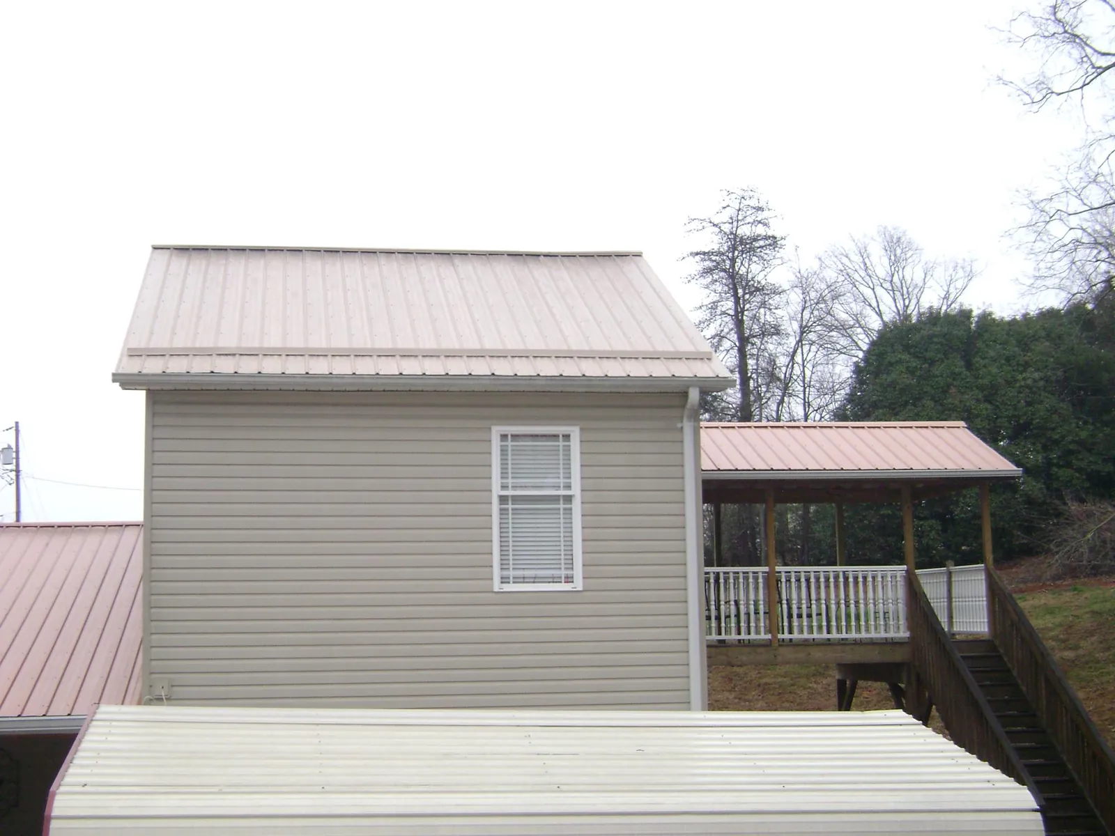 Tan metal roofs on a two story addition and attached porch, from a Roof Replacement job in Hamptonville